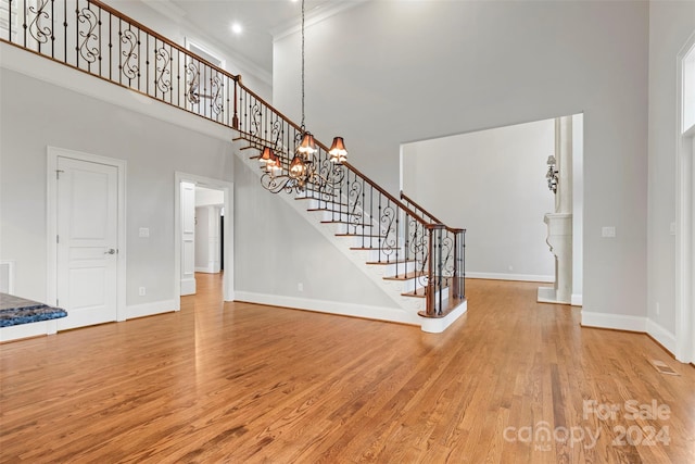 interior space with crown molding, a towering ceiling, light hardwood / wood-style flooring, and a chandelier