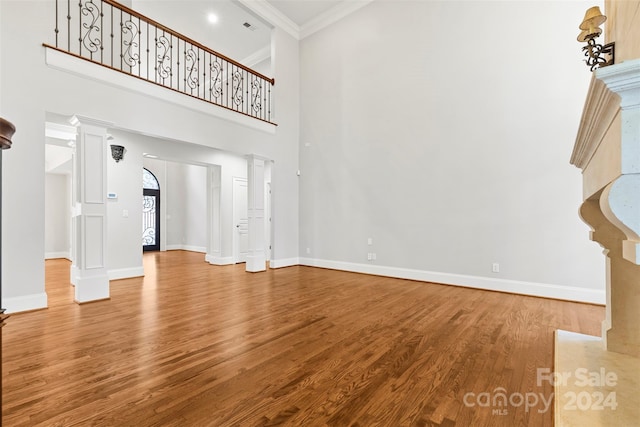 unfurnished living room with crown molding, ornate columns, hardwood / wood-style flooring, and a towering ceiling