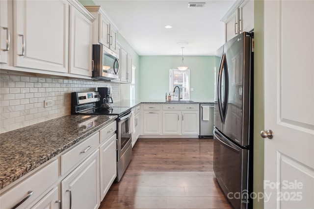 kitchen with dark wood-style floors, a sink, stainless steel appliances, white cabinetry, and backsplash