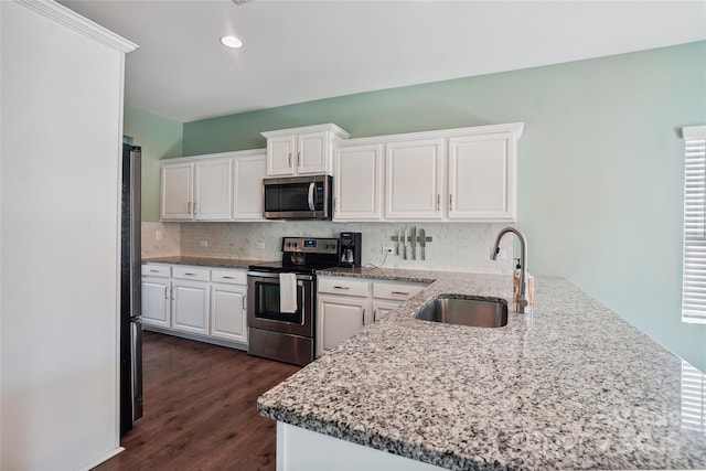 kitchen with a peninsula, a sink, white cabinetry, appliances with stainless steel finishes, and decorative backsplash