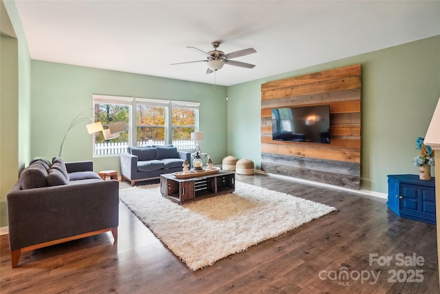 living area featuring dark wood-type flooring, baseboards, and a ceiling fan