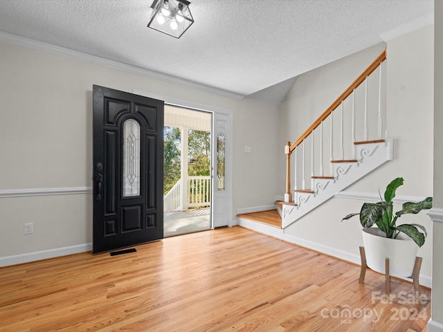 foyer entrance with ornamental molding, a textured ceiling, and light wood-type flooring