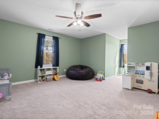 rec room with ceiling fan, a textured ceiling, and light colored carpet