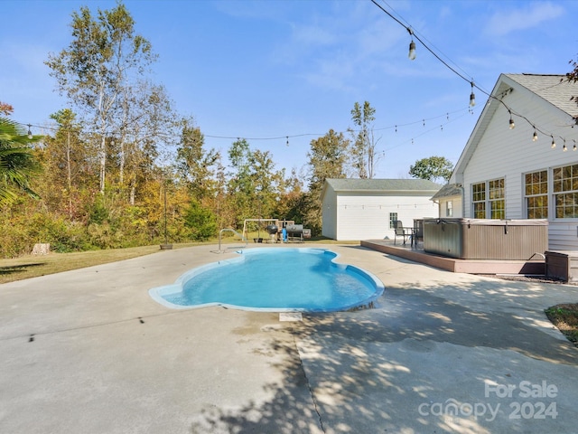 view of swimming pool featuring a hot tub, an outbuilding, a deck, and a patio