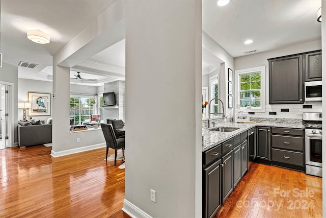 kitchen with tasteful backsplash, appliances with stainless steel finishes, light stone countertops, ceiling fan, and light hardwood / wood-style flooring