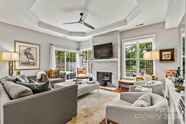 living room with a fireplace, light hardwood / wood-style floors, ceiling fan, and a raised ceiling