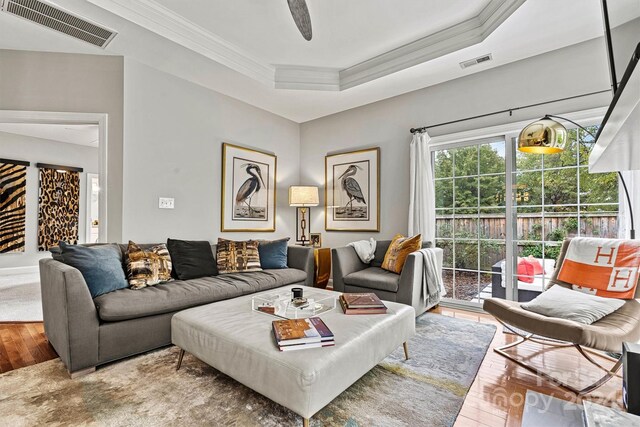 living room featuring hardwood / wood-style floors, ceiling fan, a raised ceiling, and ornamental molding