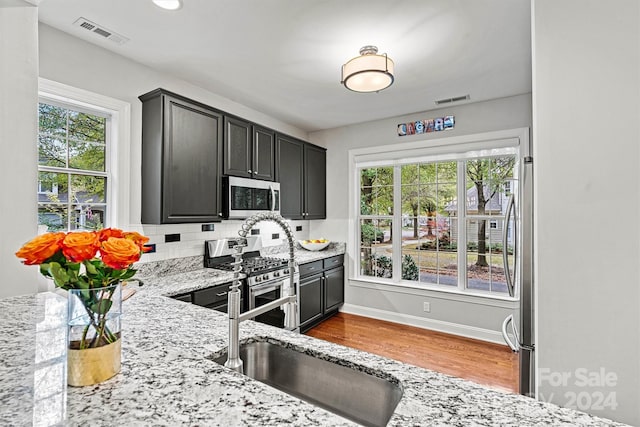 kitchen with a wealth of natural light, light stone countertops, appliances with stainless steel finishes, and backsplash