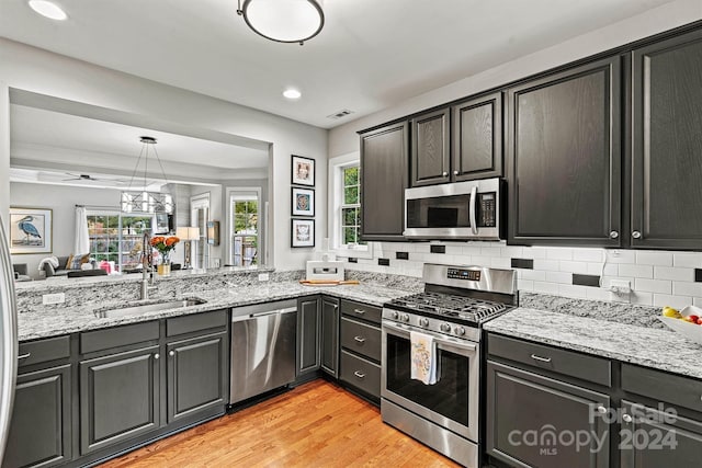 kitchen with stainless steel appliances, light hardwood / wood-style floors, light stone counters, decorative backsplash, and hanging light fixtures