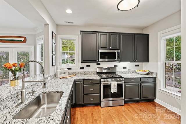 kitchen featuring stainless steel appliances, sink, ornamental molding, tasteful backsplash, and light hardwood / wood-style flooring