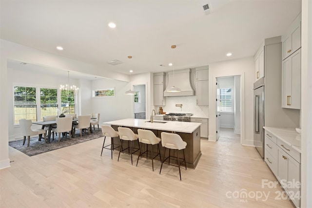 kitchen with light hardwood / wood-style flooring, a healthy amount of sunlight, custom exhaust hood, and an island with sink