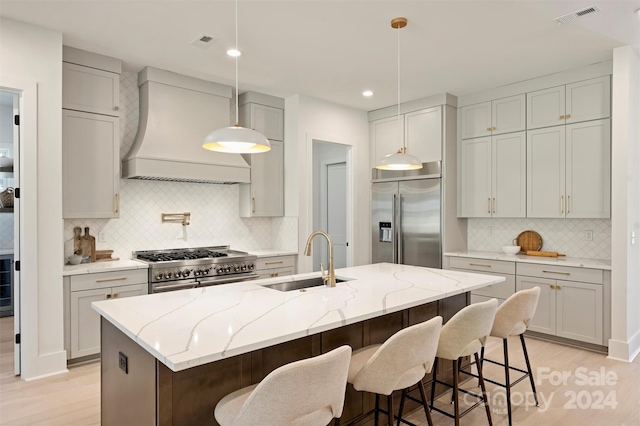 kitchen with sink, light stone countertops, high end appliances, custom exhaust hood, and a kitchen island with sink