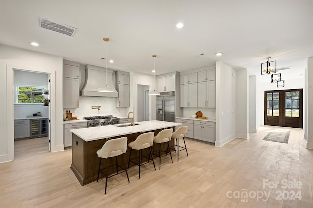 kitchen featuring a kitchen bar, custom exhaust hood, an island with sink, light hardwood / wood-style flooring, and premium appliances