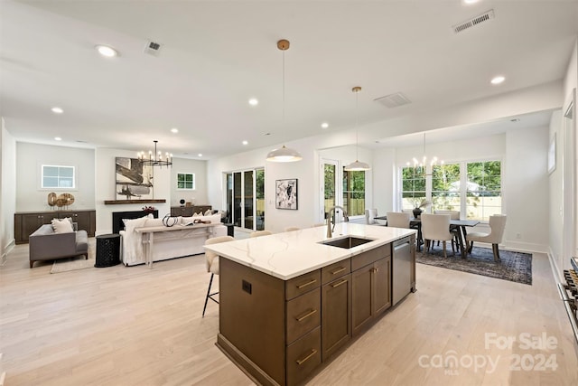 kitchen featuring light stone counters, decorative light fixtures, sink, stainless steel dishwasher, and light hardwood / wood-style flooring