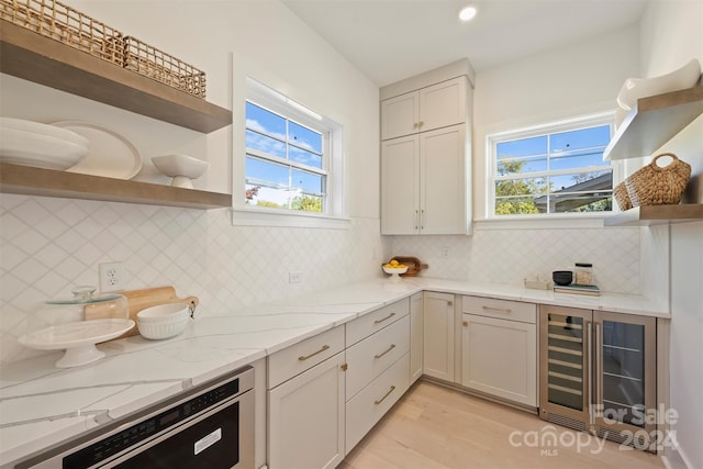 kitchen featuring stainless steel dishwasher, beverage cooler, decorative backsplash, and light stone counters