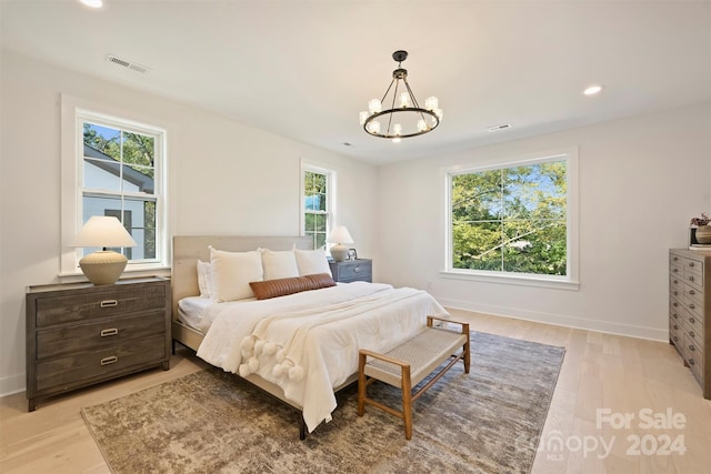 bedroom with multiple windows, an inviting chandelier, and light hardwood / wood-style floors