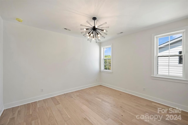 unfurnished room featuring light hardwood / wood-style flooring, a notable chandelier, and plenty of natural light