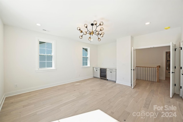 spare room featuring wine cooler, light hardwood / wood-style flooring, and a notable chandelier