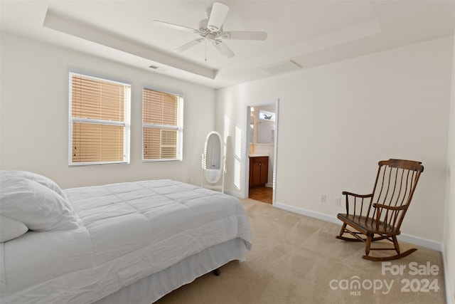 bedroom featuring ceiling fan, a raised ceiling, light carpet, and ensuite bath