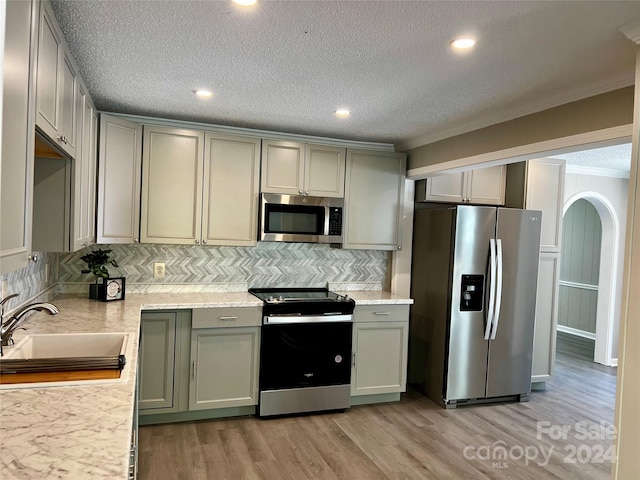 kitchen featuring appliances with stainless steel finishes, a textured ceiling, light hardwood / wood-style flooring, ornamental molding, and sink