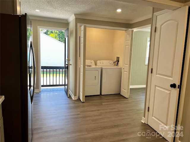 clothes washing area featuring crown molding, a textured ceiling, washer and clothes dryer, and wood-type flooring