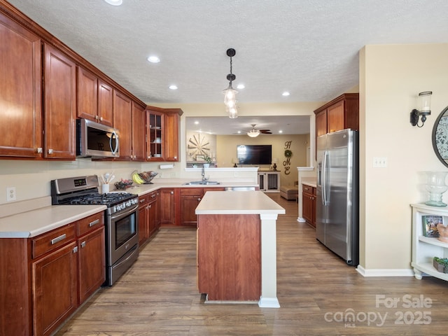 kitchen with sink, hardwood / wood-style floors, stainless steel appliances, a kitchen island, and decorative light fixtures