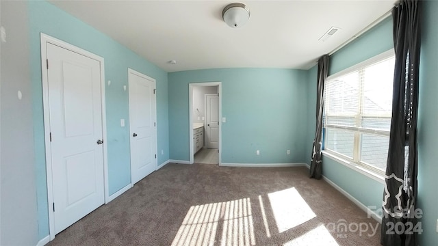 unfurnished bedroom with dark colored carpet and ensuite bathroom