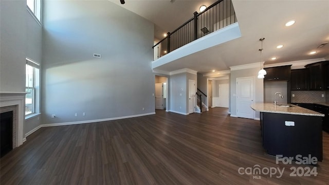 kitchen with a towering ceiling, dark hardwood / wood-style floors, sink, and a center island with sink