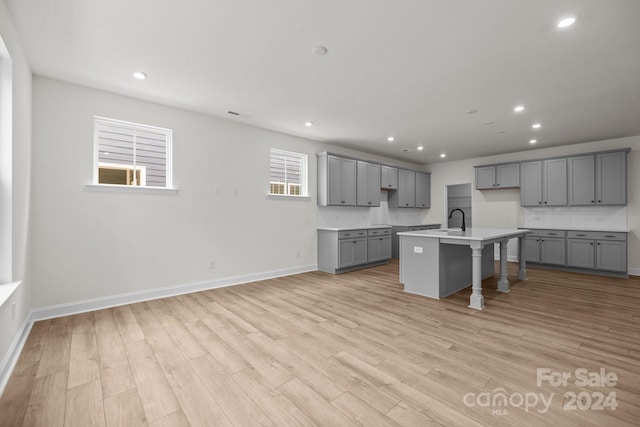 kitchen with gray cabinets, a center island with sink, and light wood-type flooring