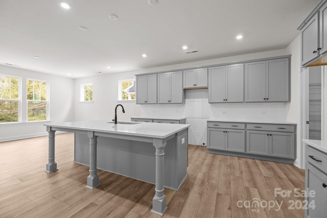 kitchen with gray cabinetry, light wood-type flooring, and a kitchen island with sink