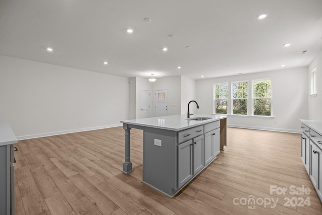 kitchen featuring sink, a breakfast bar, an island with sink, light hardwood / wood-style flooring, and gray cabinetry