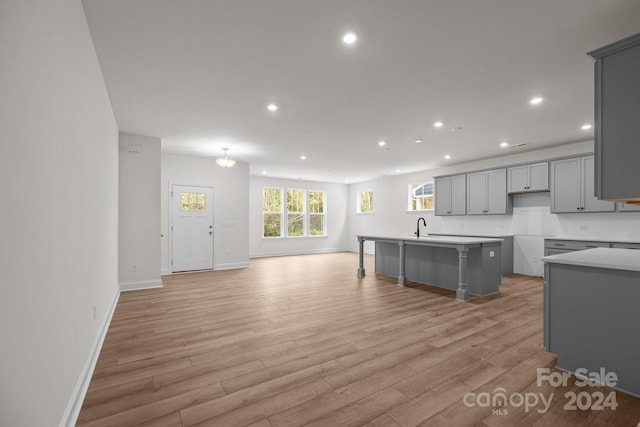 kitchen with gray cabinetry, a center island with sink, a kitchen bar, sink, and light hardwood / wood-style floors