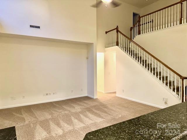 unfurnished living room with a towering ceiling, carpet, and ceiling fan