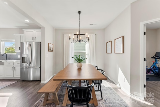 dining space with dark wood-type flooring, an inviting chandelier, and sink