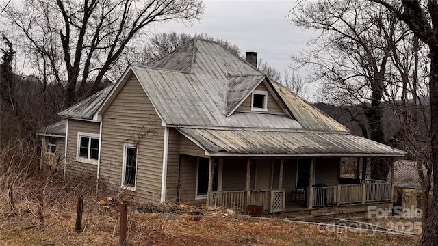 view of front of house with covered porch, a chimney, and metal roof