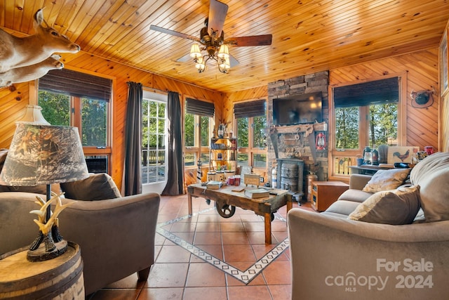 tiled living room with wood ceiling, a stone fireplace, wooden walls, and ceiling fan