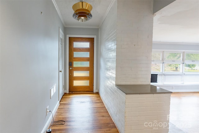 entryway featuring ornamental molding, brick wall, and light wood-type flooring