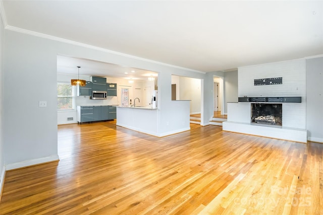 unfurnished living room featuring crown molding, sink, a fireplace, and light wood-type flooring