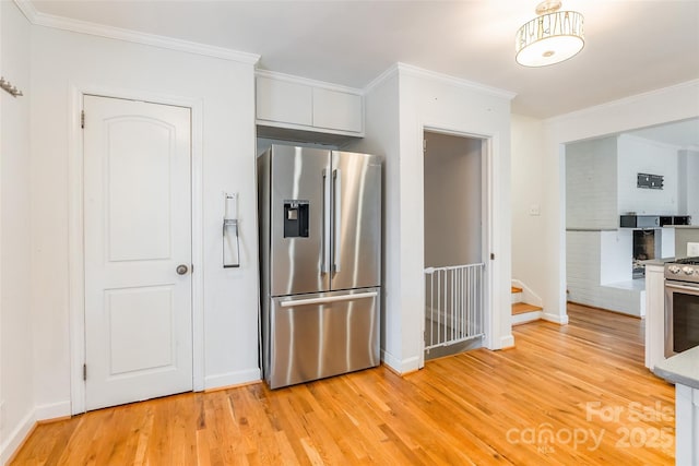 kitchen with light wood-type flooring, ornamental molding, white cabinets, and appliances with stainless steel finishes