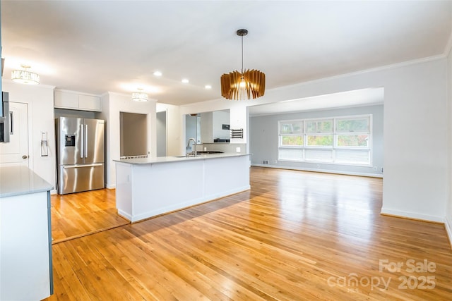 kitchen with stainless steel refrigerator with ice dispenser, ornamental molding, white cabinets, decorative light fixtures, and light wood-type flooring