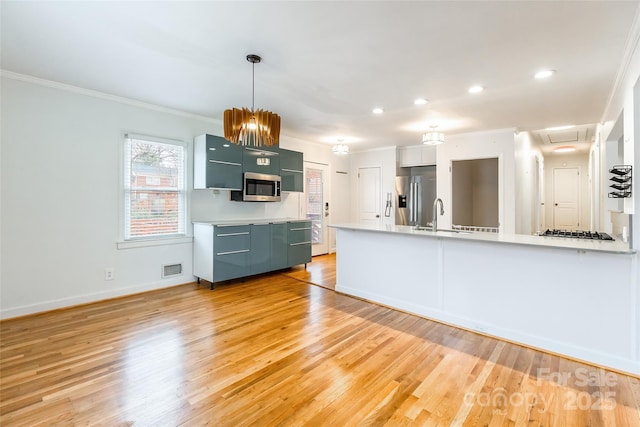 kitchen featuring decorative light fixtures, sink, ornamental molding, stainless steel appliances, and light hardwood / wood-style flooring