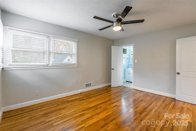 unfurnished bedroom with ceiling fan, ensuite bathroom, a textured ceiling, and light wood-type flooring