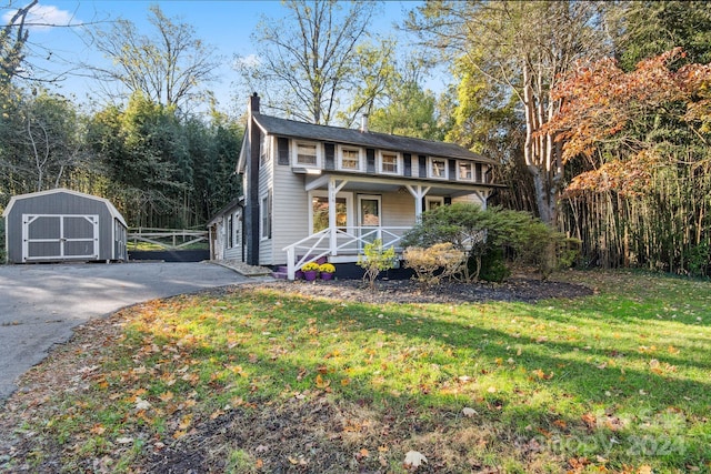 view of front of home featuring covered porch, a storage shed, and a front lawn