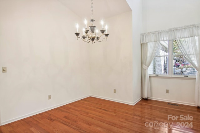 empty room with lofted ceiling, a notable chandelier, and hardwood / wood-style flooring