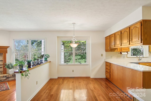 kitchen with kitchen peninsula, a textured ceiling, light hardwood / wood-style flooring, pendant lighting, and sink