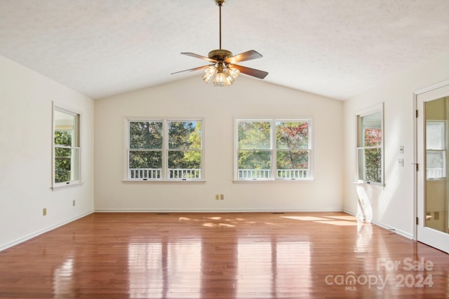 unfurnished room featuring a healthy amount of sunlight, a textured ceiling, vaulted ceiling, and light wood-type flooring