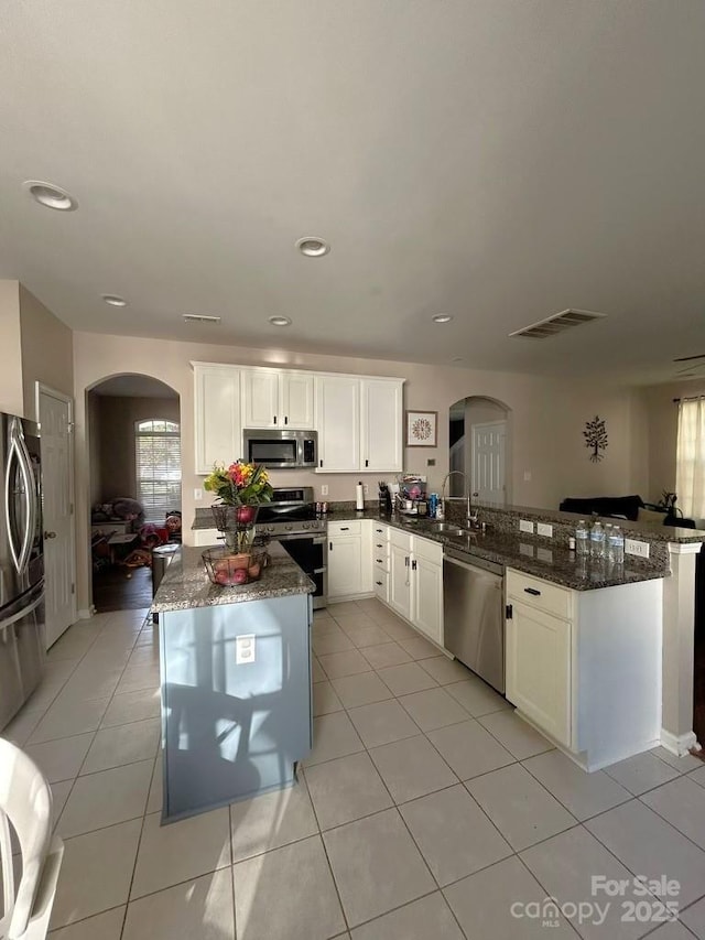 kitchen featuring kitchen peninsula, dark stone countertops, appliances with stainless steel finishes, light tile patterned flooring, and white cabinetry