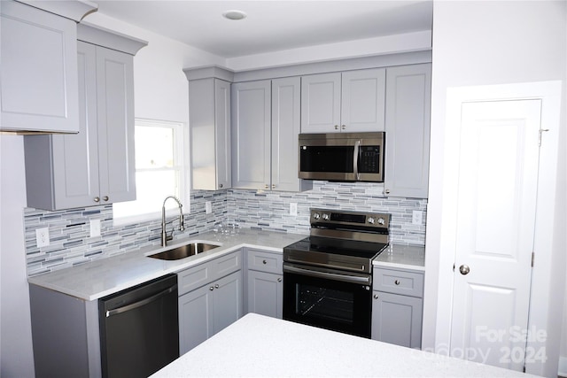 kitchen with a sink, gray cabinets, decorative backsplash, and stainless steel appliances