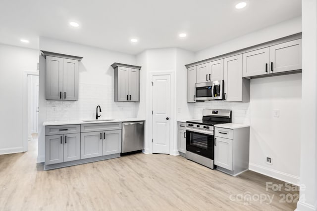 kitchen with sink, appliances with stainless steel finishes, gray cabinetry, and light hardwood / wood-style floors