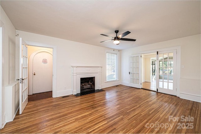 unfurnished living room featuring wood-type flooring, ceiling fan, and a brick fireplace